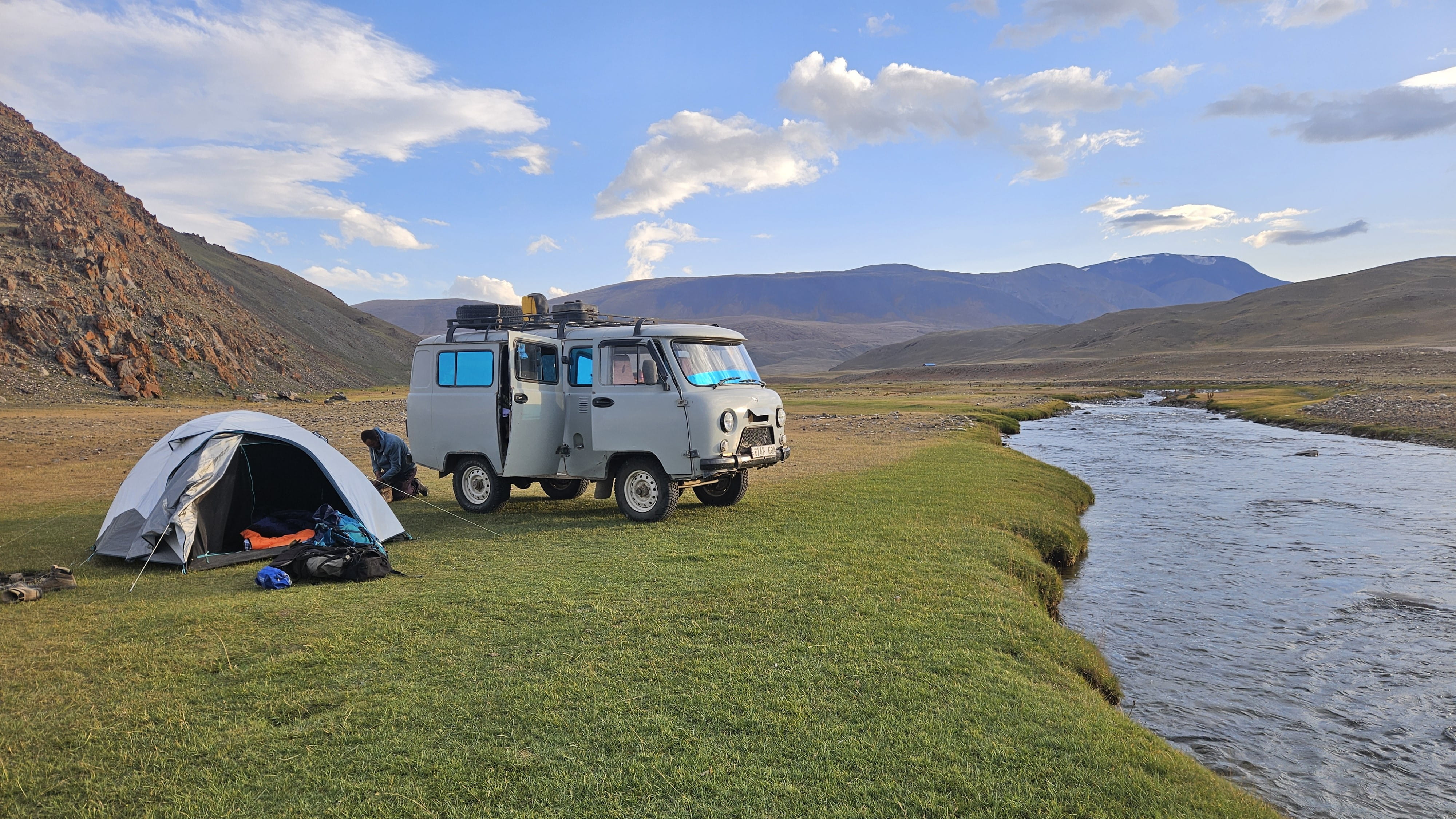 A Soviet truck parked near a tent and river deep in the Central Asian wilderness.