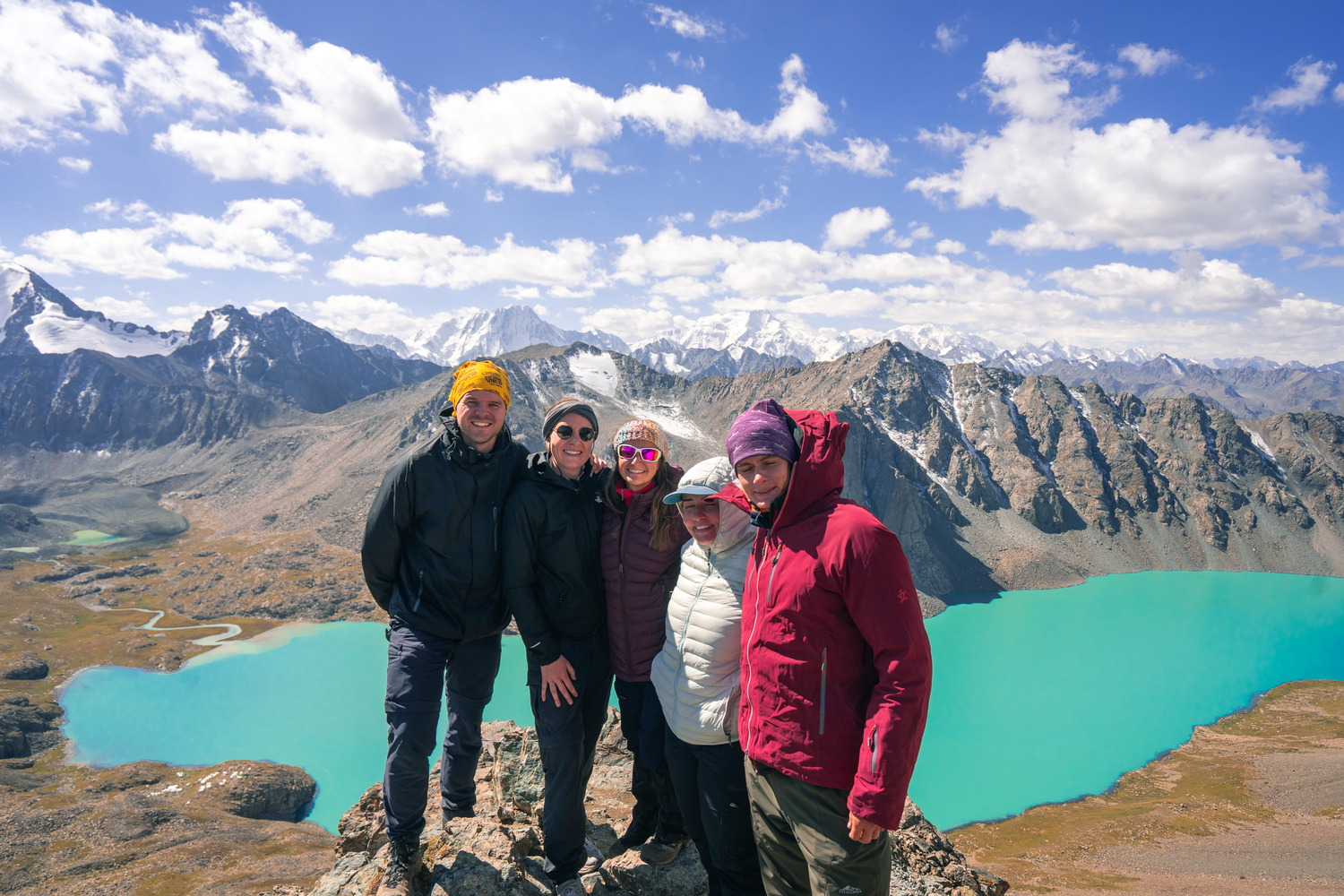 Trekkers hiking up a rocky pass with the turqouise alpine lake Ala-Kul behind them.
